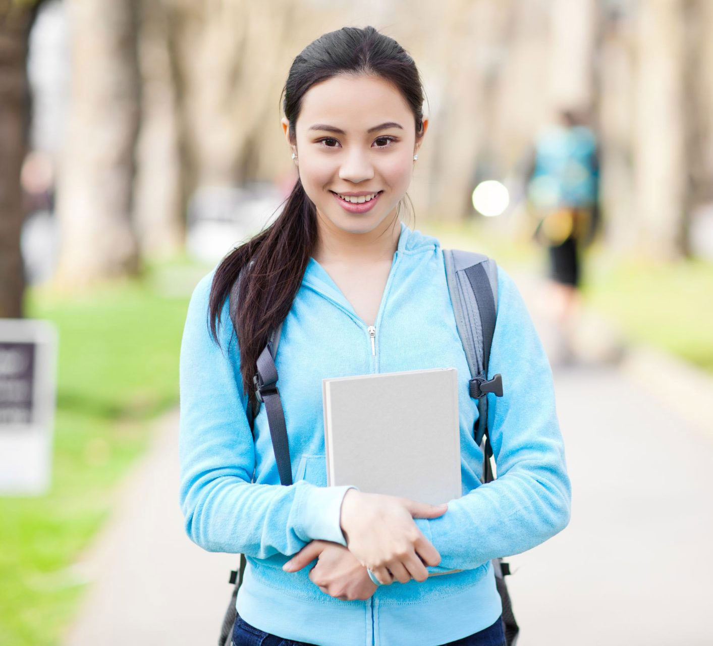 an Asian college student with a backpack and notebook smiles on a college campus
