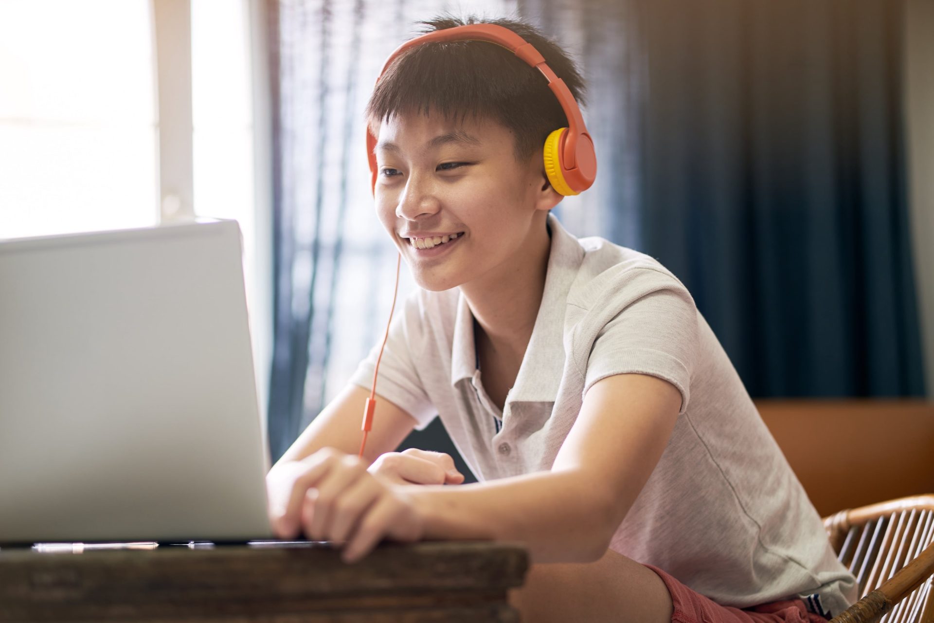 an Asian student wearing headphones smiles looking at his laptop