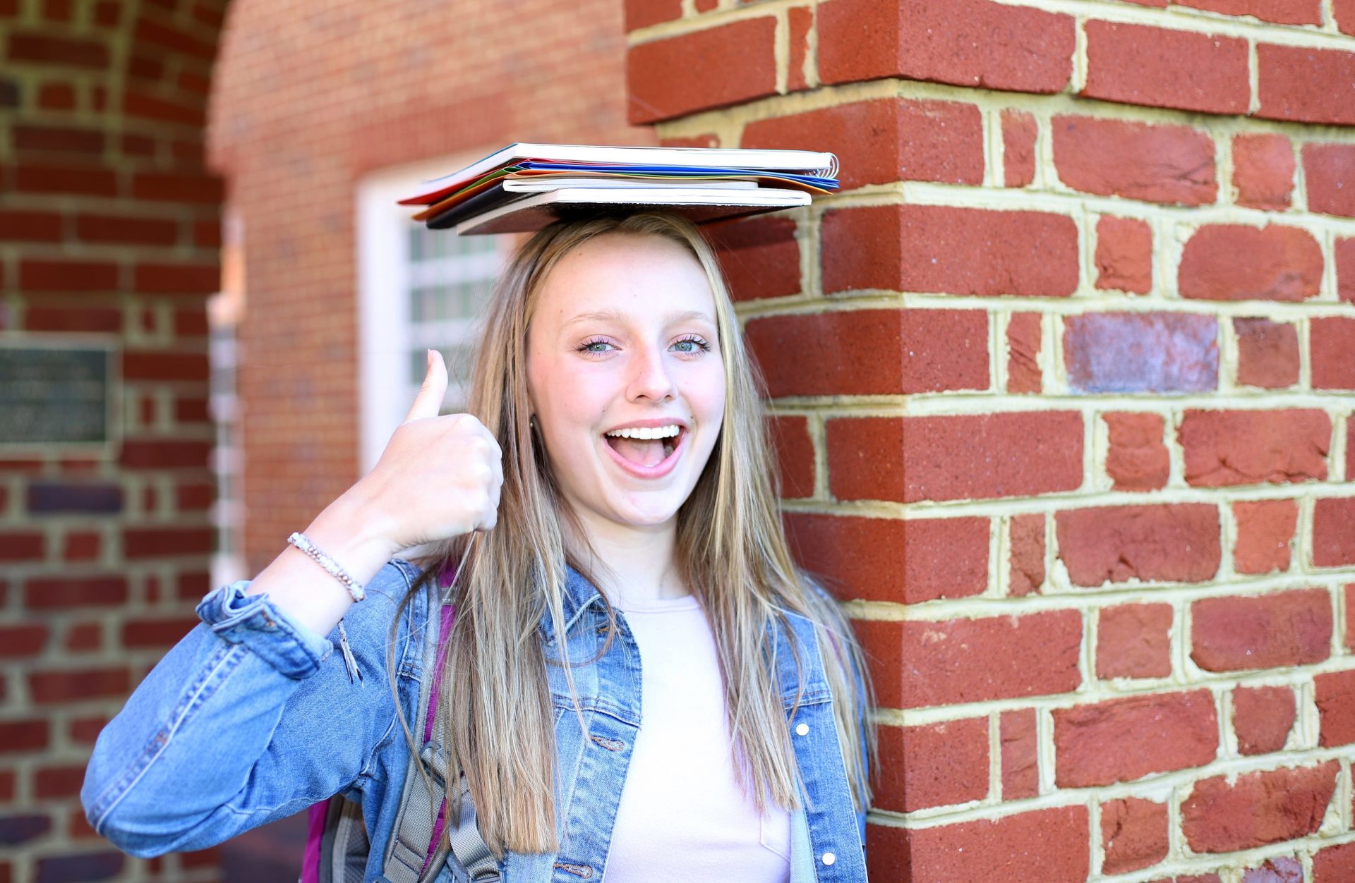 a woman gives a thumbs up to the camera with notebooks on her head