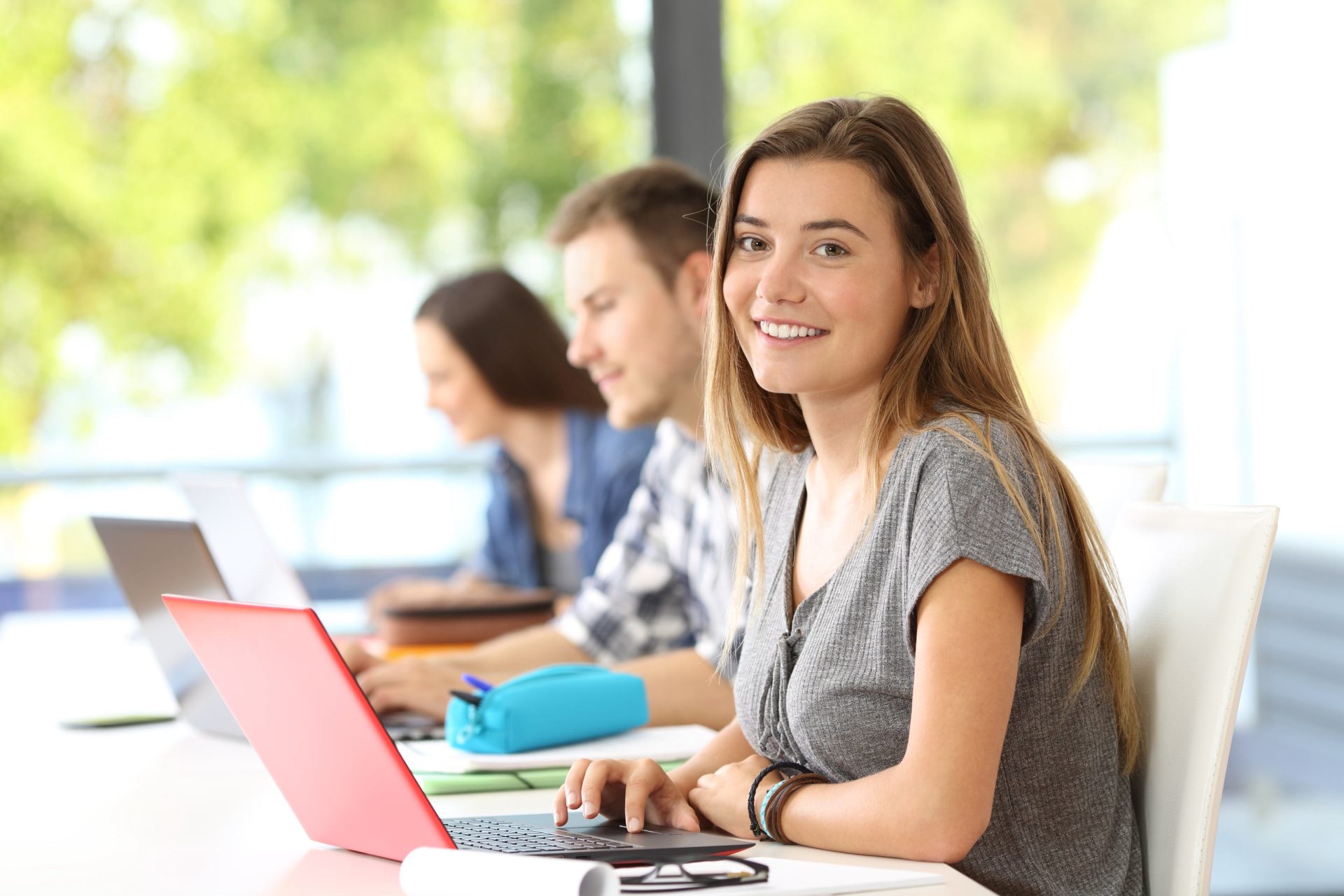 multiple college-age students work on laptops in a sunny room