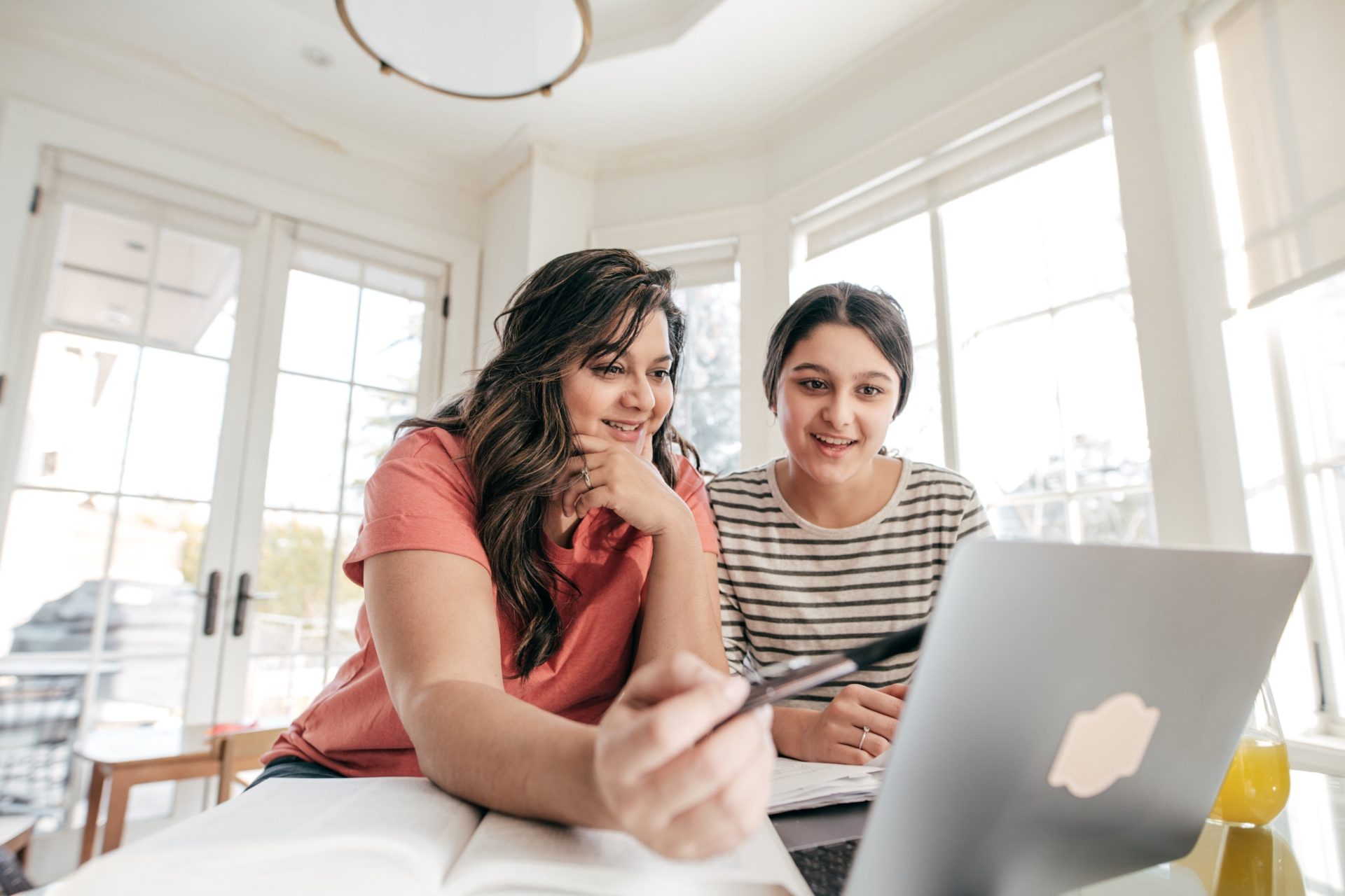 a mother and daughter sit at a kitchen table discussing information on a laptop